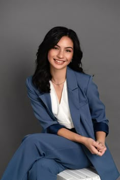 a woman sitting on top of a white box wearing a blue suit and smiling at the camera