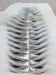 a close up of a metal object on a white tablecloth with silver foiled leaves