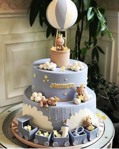 a three tiered cake with teddy bears on top and an air balloon above it