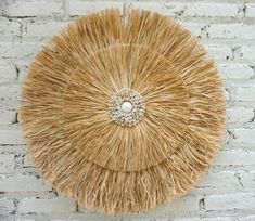 a round straw bag hanging on a white brick wall with a beaded brooch in the center