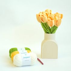 a white vase filled with yellow flowers next to a crochet yarn skein