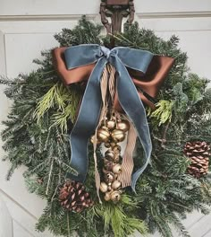 a christmas wreath with bells and pine cones hanging on the front door, decorated with blue ribbon