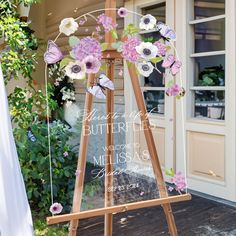 an easel with flowers and butterflies on it sitting in front of a door way