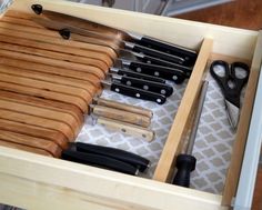 an open drawer with knives and other kitchen utensils in it on a table