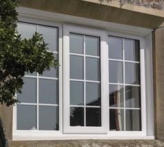 an open window on the side of a stone building next to a tree and shrub