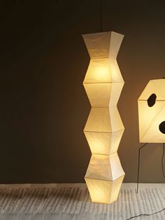 two lamps sitting next to each other on top of a carpeted floor in front of a wall