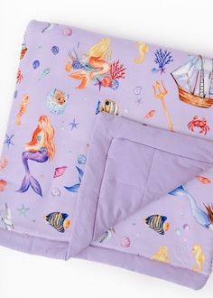 a purple blanket with mermaids and sea animals on it is laying next to a pillow