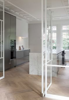 an empty room with white walls and wooden floors is shown in this image, there are glass doors that open to reveal the kitchen