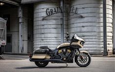 a gold and black motorcycle parked in front of a silo with grain tanks behind it