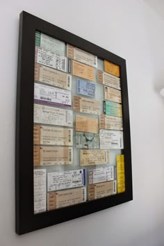 a black frame filled with lots of different types of tickets on a wall next to a lamp