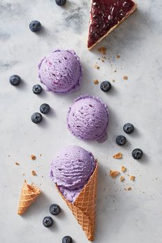 three scoops of blueberry ice cream next to two slices of pie on a table