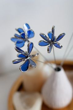 two blue glass flowers are in a white vase on a table next to an object