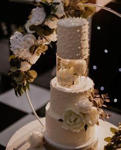 a three tiered white wedding cake with flowers on the top and bottom, sitting on a checkered tablecloth