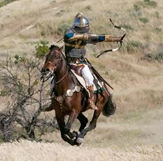 a man in armor riding on the back of a brown horse while holding a bow and arrow