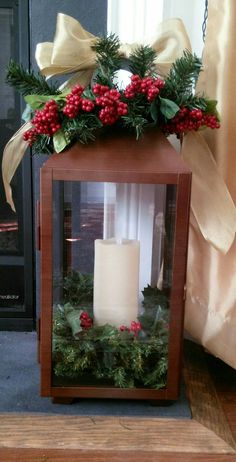 a lighted lantern with holly and red berries on it sitting on a wooden floor next to a window