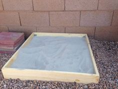 a sand box sitting on top of gravel next to a brick wall and two boxes