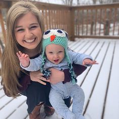 a woman holding a baby wearing a knit owl hat