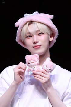 a person holding two stuffed animals in front of their face and wearing a pink hat