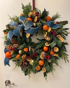 a christmas wreath hanging on the wall with oranges and greenery in front of it