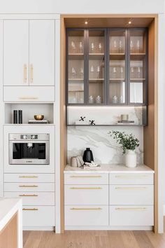 a kitchen with white cabinets and marble counter tops, gold trim on the glass doors