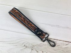 a leather keychain with an ornate design on the front and side, sitting on a white wooden surface