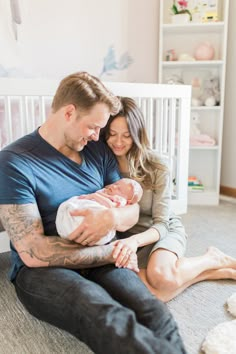 a man and woman sitting on the floor holding a baby