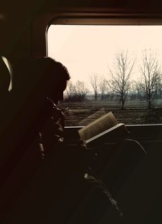 a person sitting on a train with an open book in their lap and looking out the window