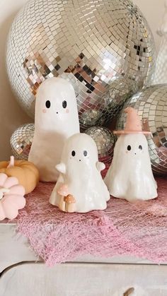 three white ghost figurines sitting on top of a table next to disco balls