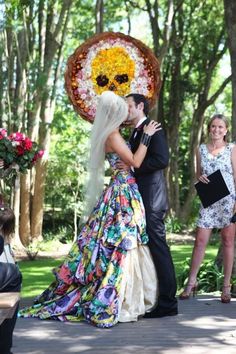 a bride and groom kissing in front of a floral skull decoration on their wedding day