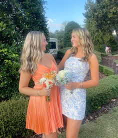 two beautiful women standing next to each other in front of some bushes and trees with flowers