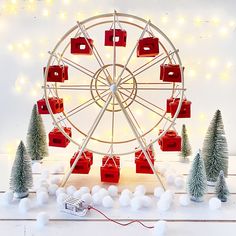 a ferris wheel with christmas trees and lights around it in front of a white wall