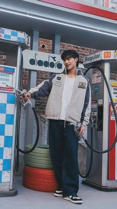 a man standing in front of a gas station with his hands on the hoses