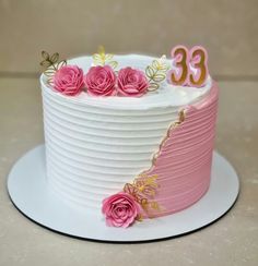 a white cake with pink frosting and gold numbers on the top is decorated with roses