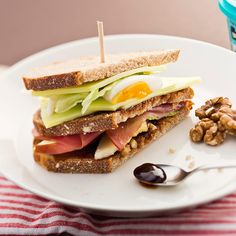 a white plate topped with a cut in half sandwich next to walnuts and an egg