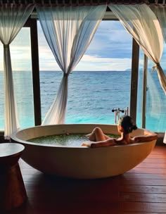 a woman laying in a large bathtub next to the ocean