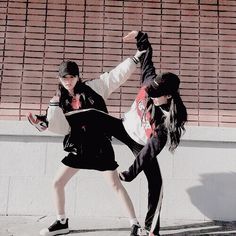 two young women are dancing on the sidewalk in front of a brick wall and building