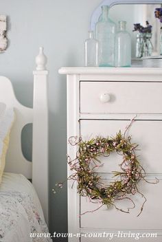 a white dresser with a wreath on top of it next to a bed and mirror