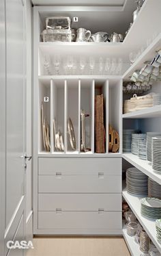 a white cupboard filled with lots of dishes and silverware next to shelves full of glasses