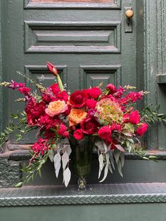 a vase filled with red and pink flowers sitting in front of a green painted door