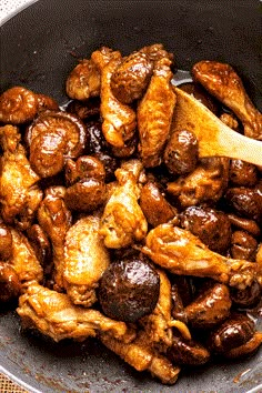 chicken and mushrooms cooking in a skillet with a wooden spoon on the side,