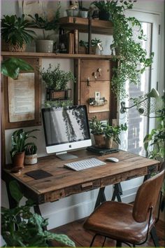 a wooden desk topped with a computer monitor next to a plant filled window sill