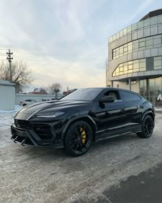 a black sports car is parked in front of a large building with glass windows and snow on the ground