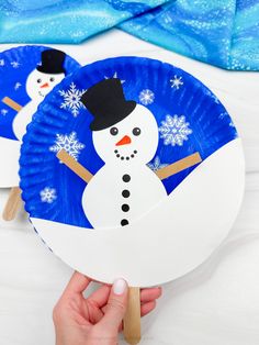 two paper plates with snowmen on them, one is holding a fan and the other has a stick