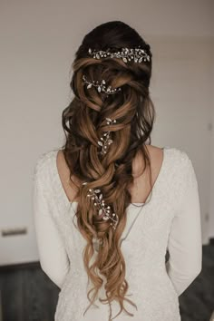 a woman with long hair wearing a white top and some flowers in her hair is shown from the back