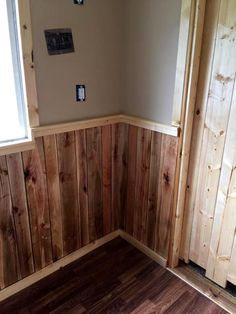 an empty room with wood paneling on the walls and wooden floors in front of a window