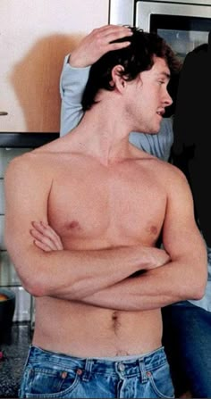 a man with his shirt off standing in front of a microwave and holding his hands on his head