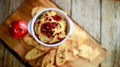 a bowl filled with hummus and pomegranate on top of crackers