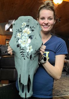 a woman holding up a skull with flowers painted on it