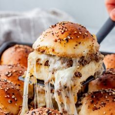 a person is lifting some sliders out of the pan with cheese and sauce on them