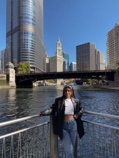 a woman standing on the edge of a bridge next to a body of water with tall buildings in the background